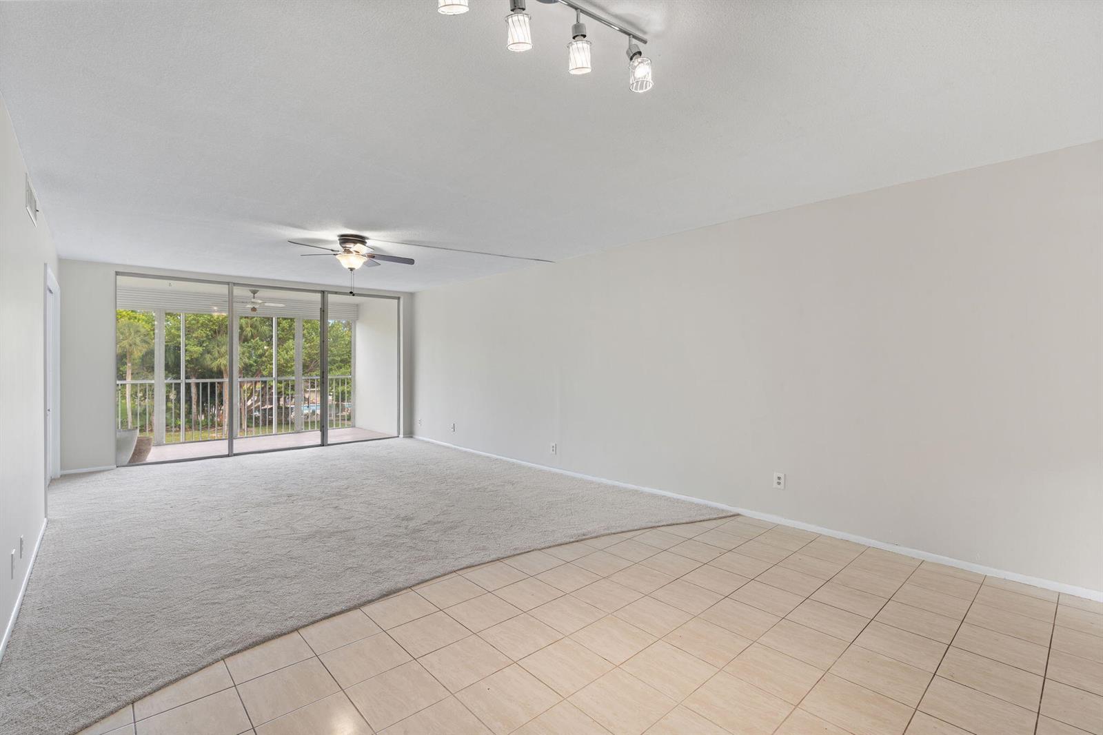A living room features beige carpeting, tile flooring, a ceiling fan, and a sliding glass door — 2650 S Course Drive Unit 308, Pompano Beach FL 33069, POMPANO BEACH, FL