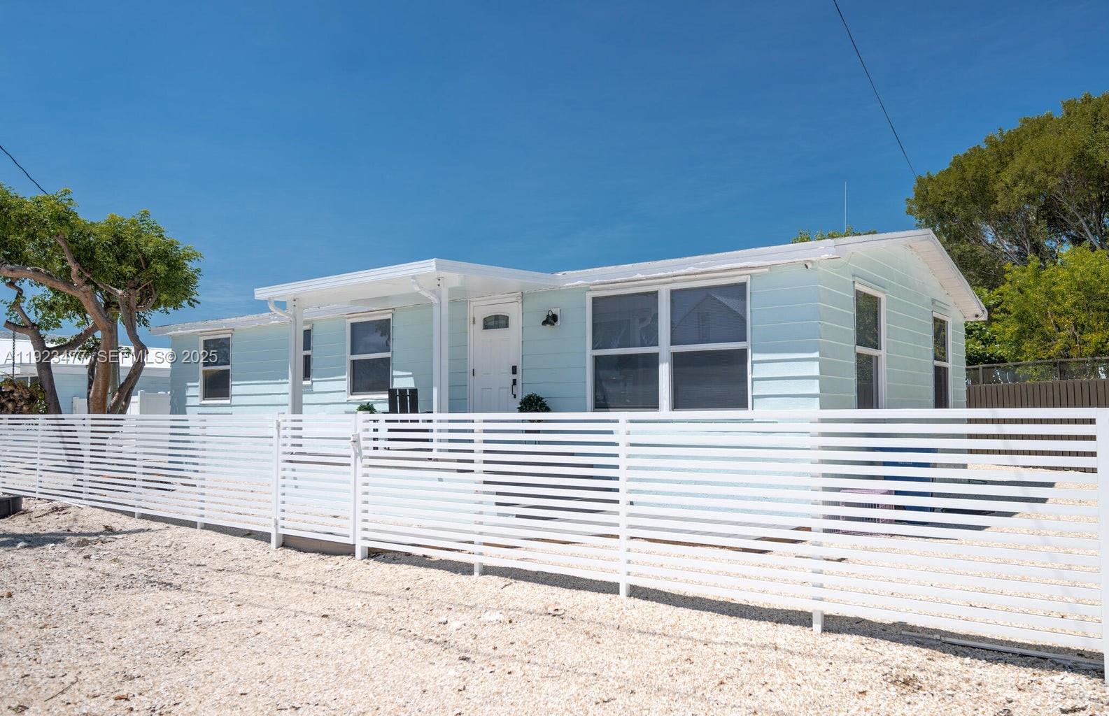 A light blue single-story house features a white horizontal slat fence in the front yard — 212 Buttonwood Ln, Key Largo FL 33070, KEY LARGO, FL