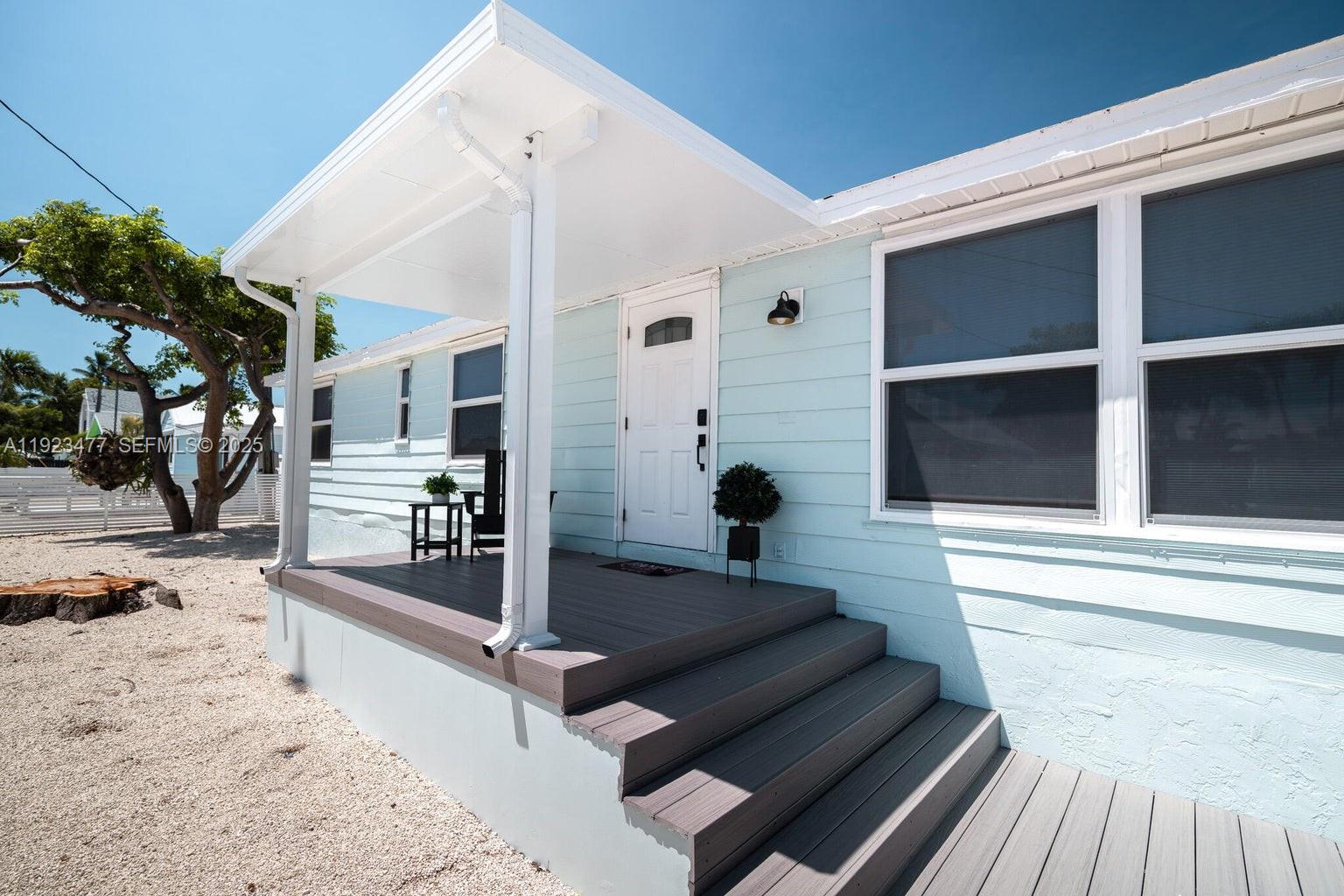 A light blue house features a covered front porch with gray composite decking and steps — 212 Buttonwood Ln, Key Largo FL 33070, KEY LARGO, FL