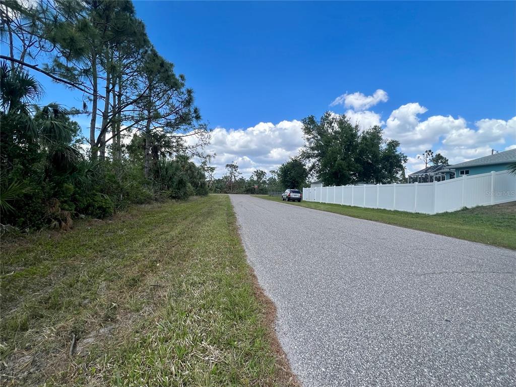 A paved road runs between a wooded area and a white vinyl fence — 4441 HOBSON STREET, PORT CHARLOTTE, FL