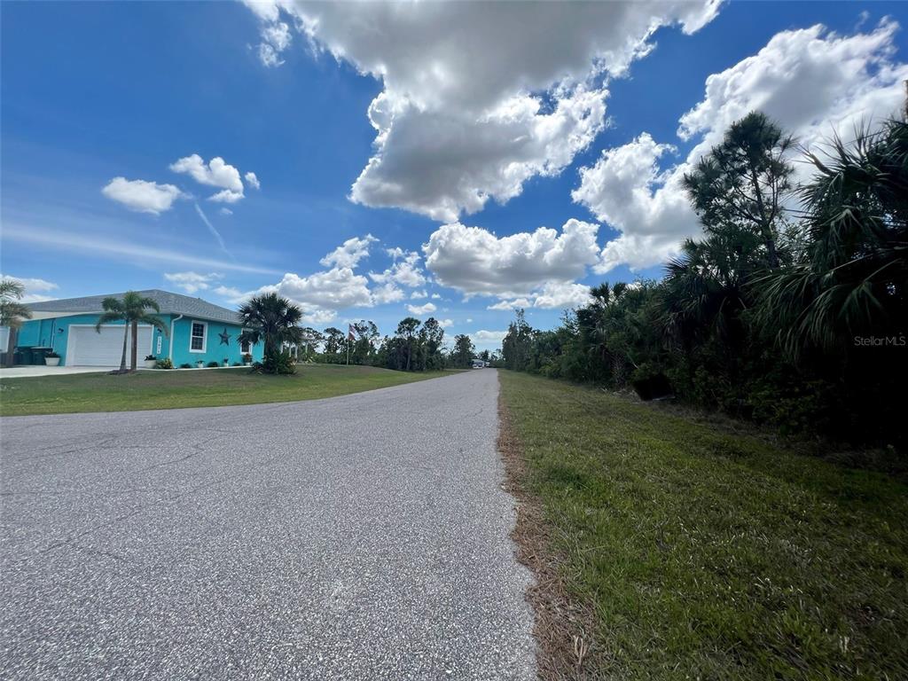 A paved road leads past a bright blue house toward a wooded area under clouds — 4441 HOBSON STREET, PORT CHARLOTTE, FL