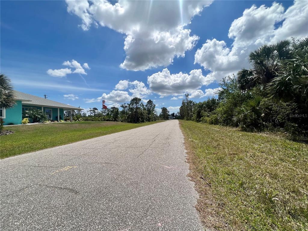 A paved road stretches toward the horizon past a teal house and dense vegetation — 4441 HOBSON STREET, PORT CHARLOTTE, FL