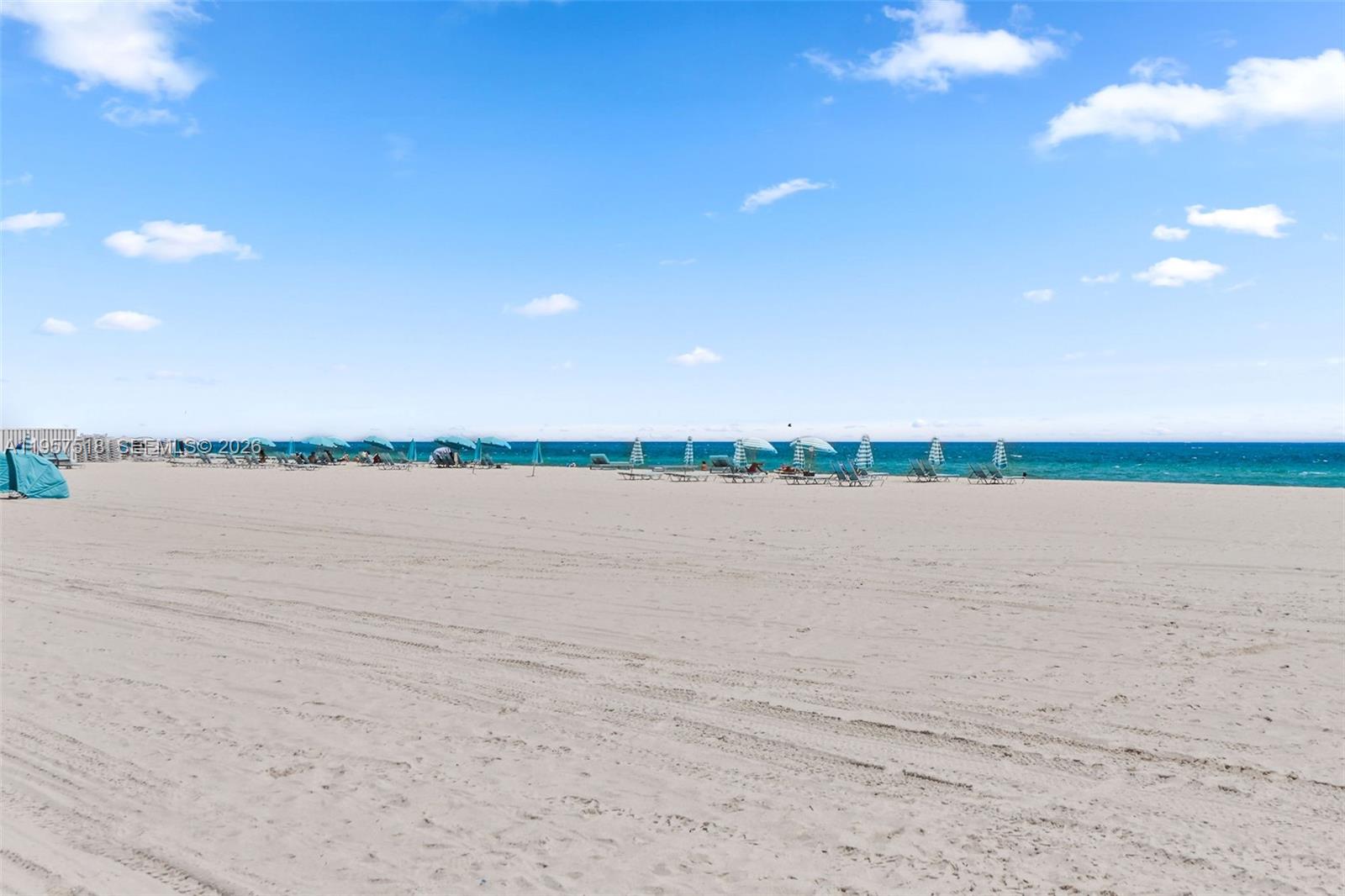 A wide, sandy beach features rows of umbrellas and lounge chairs near the ocean — 2655 Collins Ave # 2301, Miami Beach FL 33140, MIAMI BEACH, FL