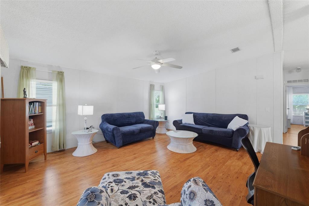 A living room features wood-look flooring, white walls, two blue sofas, and a ceiling fan — 520 TIVOLI PARK DRIVE, DAVENPORT, FL