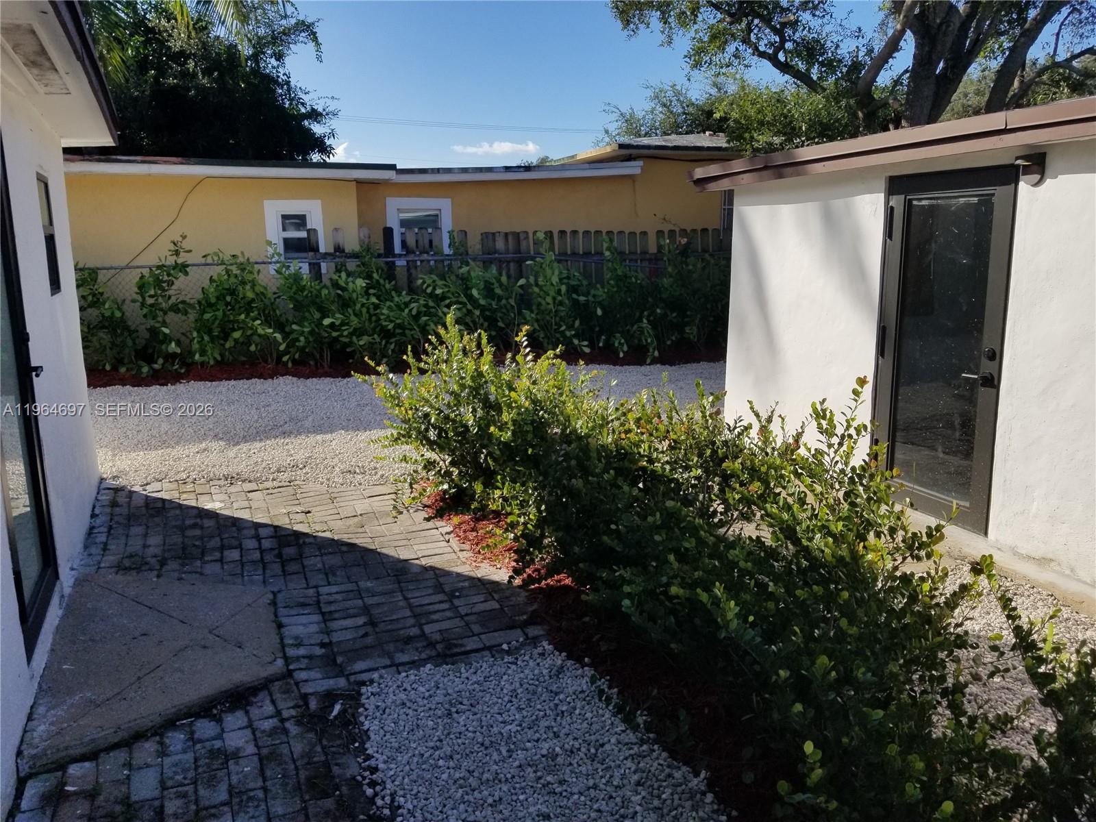 A paved walkway leads through a landscaped yard between two white exterior building walls — 1756 NW 94th St, Miami FL 33147, MIAMI, FL