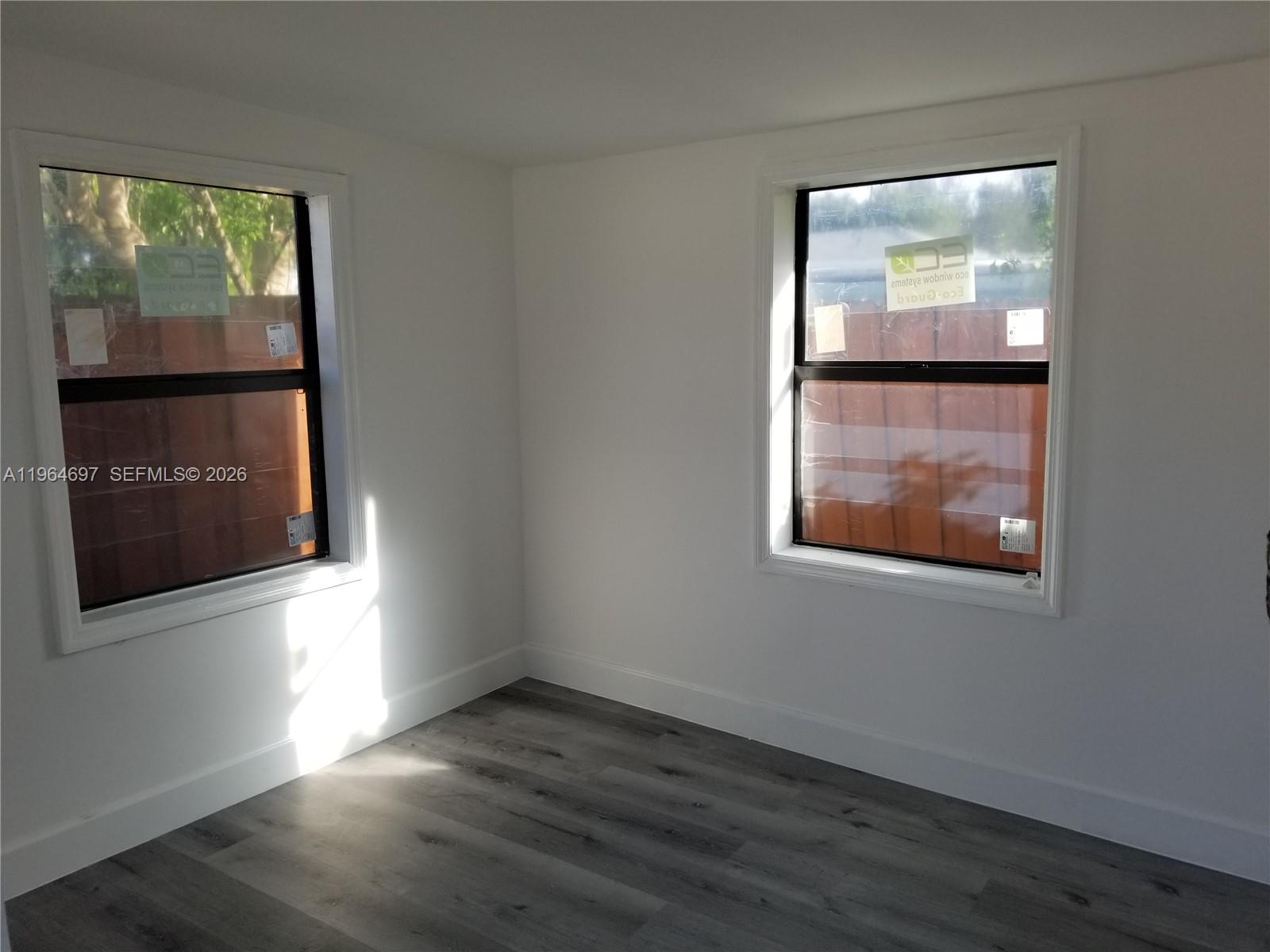 An empty room with white walls, gray wood-look flooring, and two windows facing a fence — 1756 NW 94th St, Miami FL 33147, MIAMI, FL