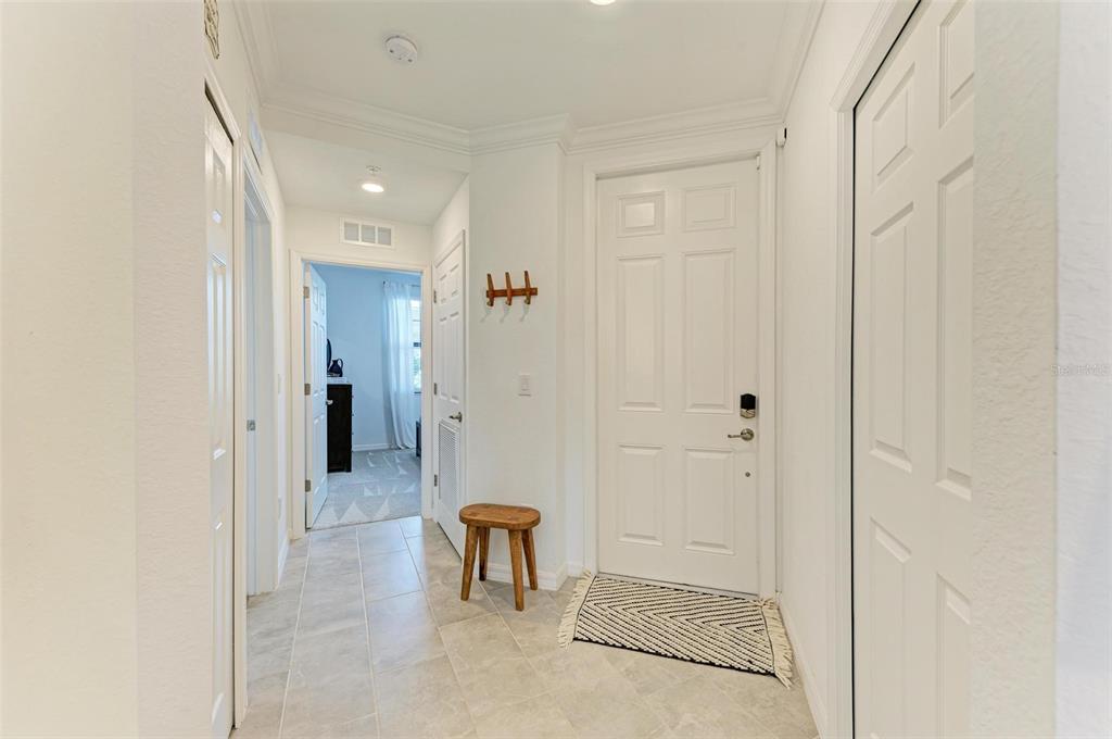 An entryway with tile flooring, a wooden stool, a coat rack, and white doors — 18114 GAWTHROP DRIVE UNIT 108, BRADENTON, FL