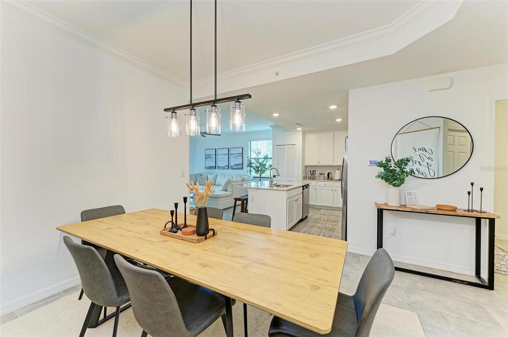 A dining area with a wooden table and pendant lighting opens into a white kitchen — 18114 GAWTHROP DRIVE UNIT 108, BRADENTON, FL