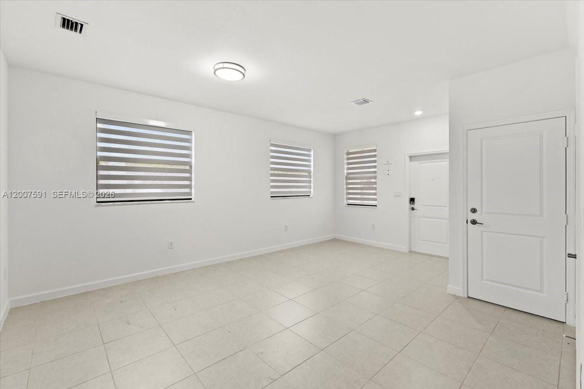 An empty room features white walls, light-colored tile flooring, two windows with blinds, and doors — 23210 SW 133rd Ct, Miami FL 33032, MIAMI, FL