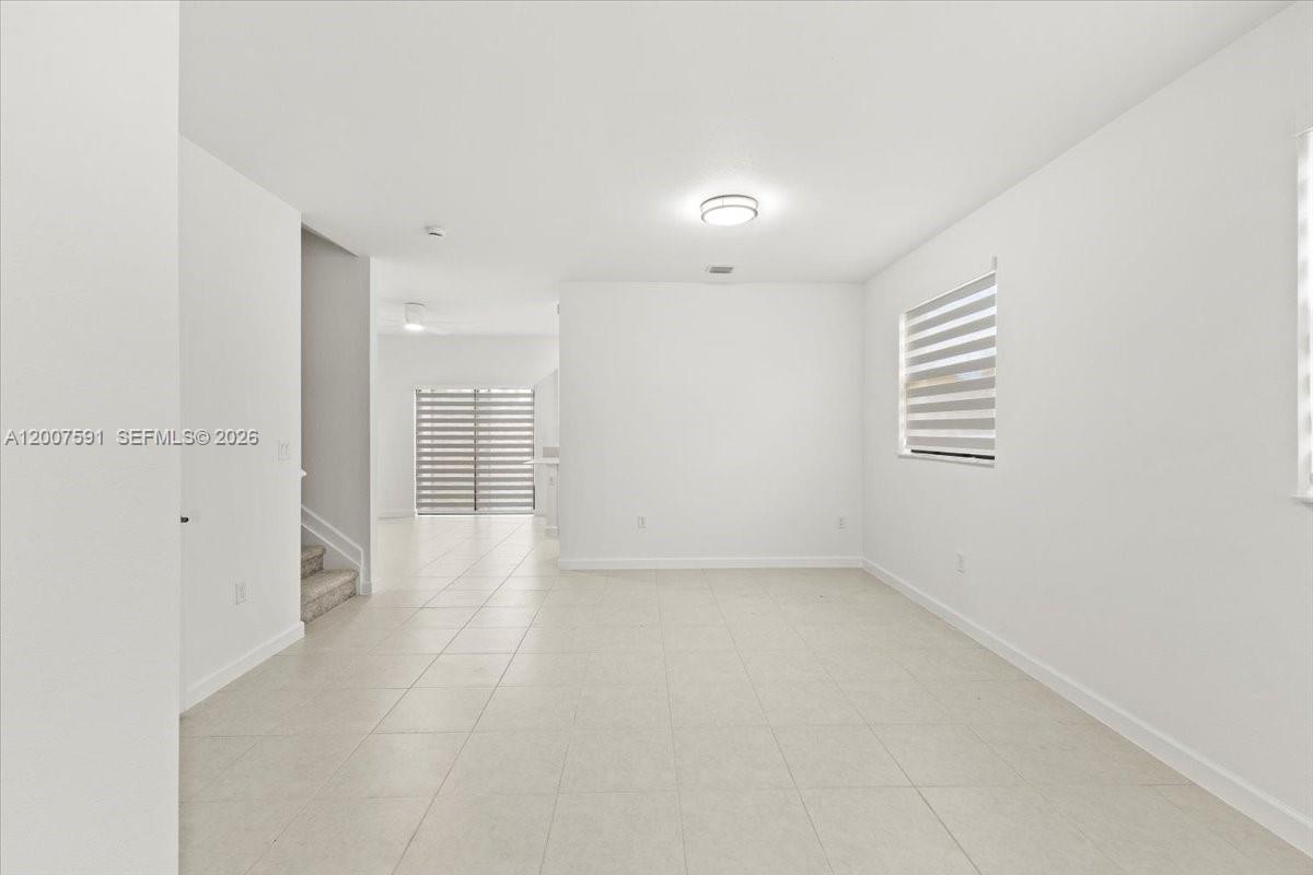 A bright, empty room features white walls, light-colored tile flooring, and a staircase — 23210 SW 133rd Ct, Miami FL 33032, MIAMI, FL