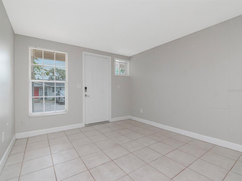An empty room with light gray walls, tile flooring, a window, and an exterior door — 104 KARDE LANE UNIT A, BRANDON, FL