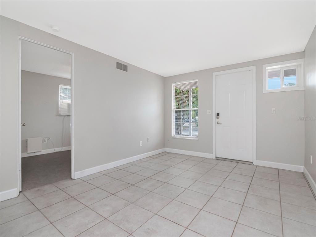 An empty room with light gray walls, tiled flooring, a white door, and a window — 104 KARDE LANE UNIT A, BRANDON, FL