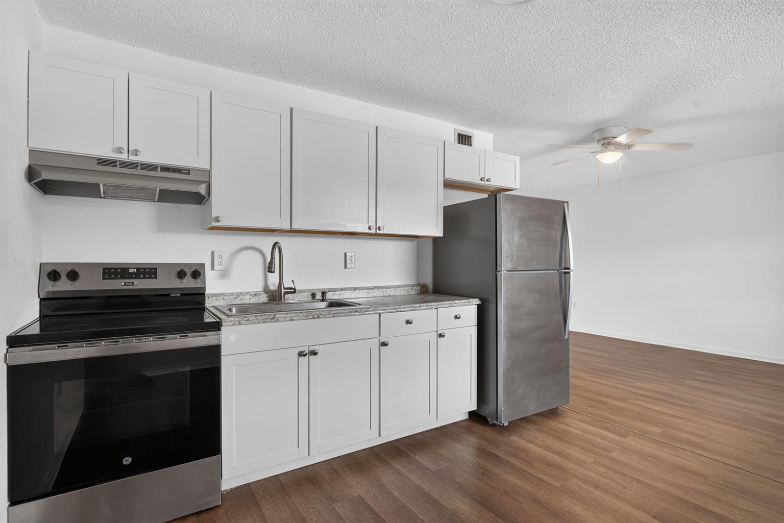 A kitchen features white cabinets, stainless steel appliances, and wood-look flooring in an open space — 1300 NW 2nd Avenue # 12, Pompano Beach FL 33060, POMPANO BEACH, FL