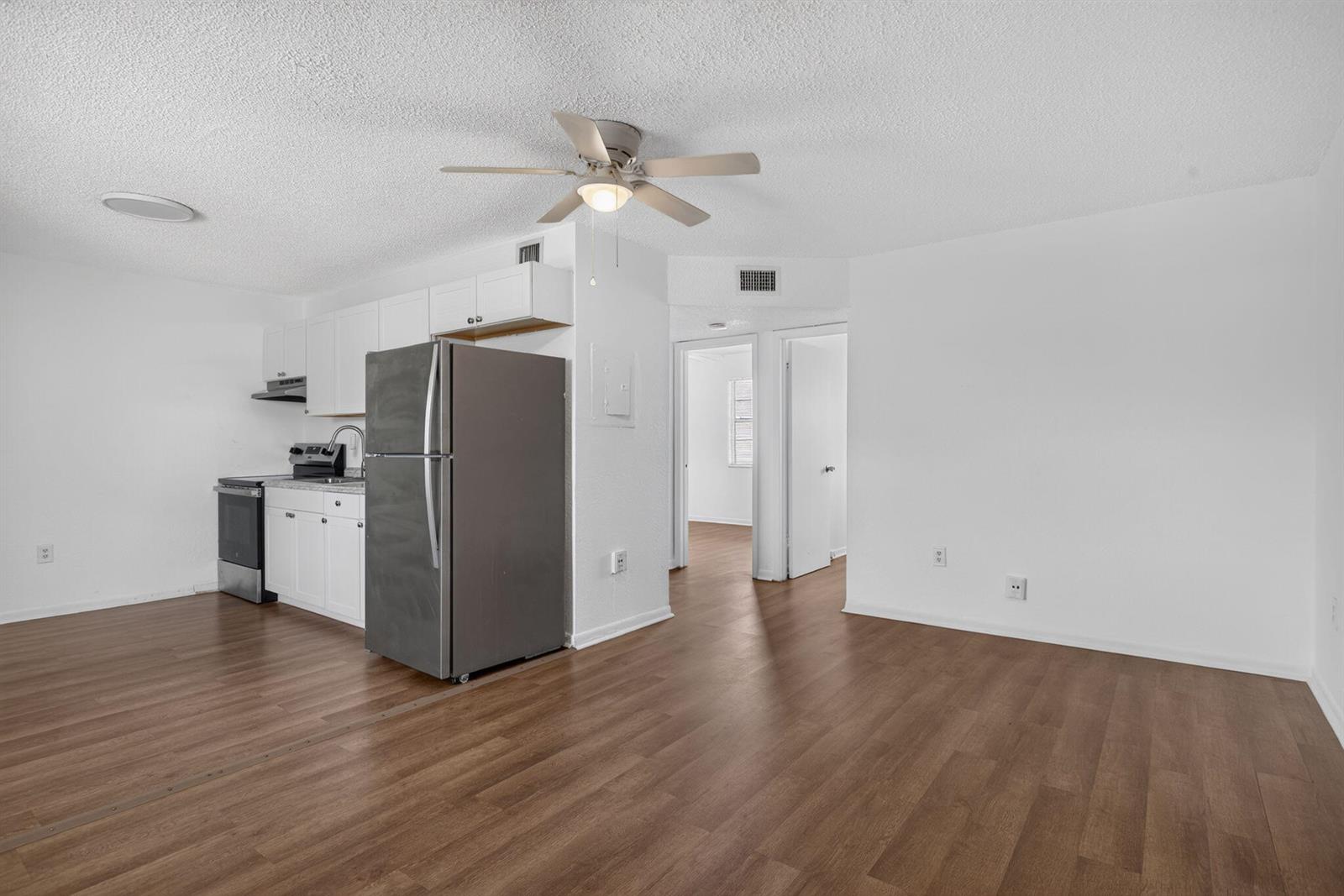 A kitchen with stainless steel appliances and white cabinets opens into a living area — 1300 NW 2nd Avenue # 12, Pompano Beach FL 33060, POMPANO BEACH, FL