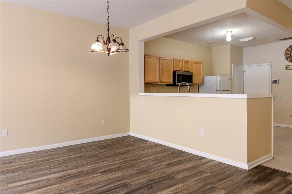 A dining area with wood-look flooring opens to a kitchen with light wood cabinets — 2720 CONCH HOLLOW DRIVE, BRANDON, FL