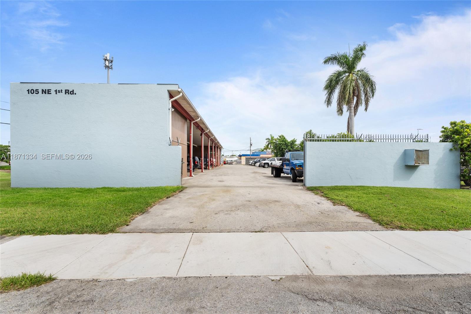 A paved driveway leads between two light blue walls toward a covered outdoor workspace — 105 NE 1st Rd, Homestead FL 33030, HOMESTEAD, FL