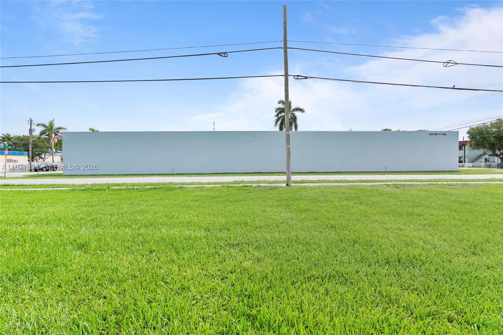A large, windowless, light-colored building stands behind a wide, grassy lawn and utility pole — 105 NE 1st Rd, Homestead FL 33030, HOMESTEAD, FL