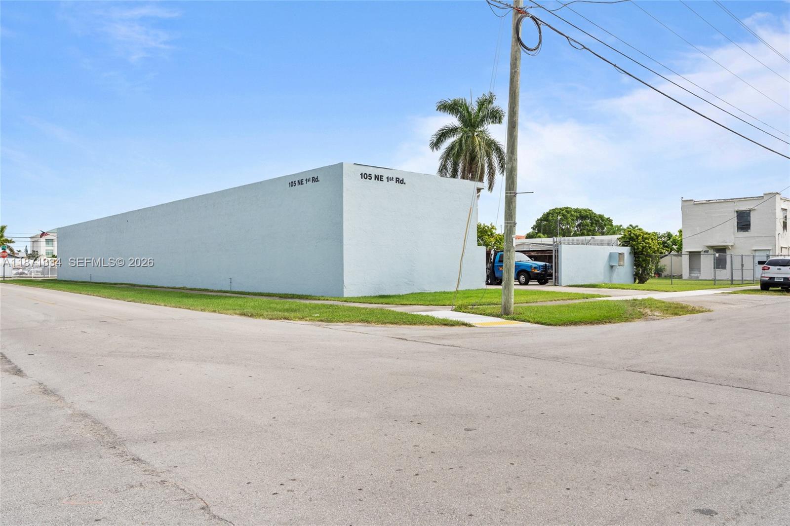 A light blue, windowless commercial building stands on a corner lot with a palm tree — 105 NE 1st Rd, Homestead FL 33030, HOMESTEAD, FL