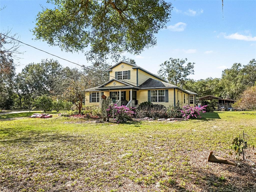 A yellow two-story house with a front porch sits on a grassy, tree-filled lot — 4400 CONRAD ACRES LANE, APOPKA, FL