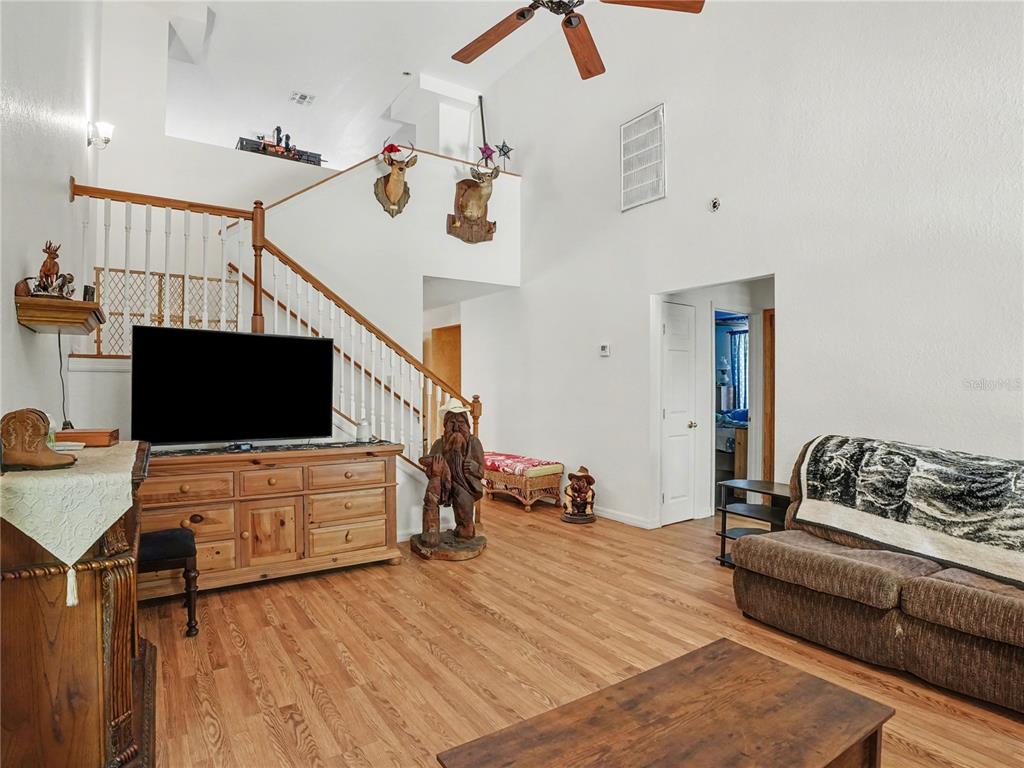 A living room features wood flooring, a staircase, a television, and vaulted ceilings — 4400 CONRAD ACRES LANE, APOPKA, FL
