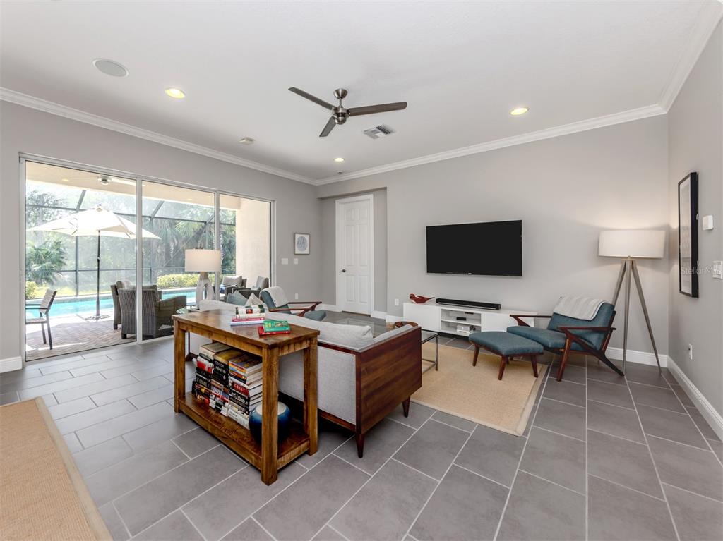 A living room features gray tile floors, a ceiling fan, a television, and sliding glass doors — 500 PADOVA WAY, NORTH VENICE, FL
