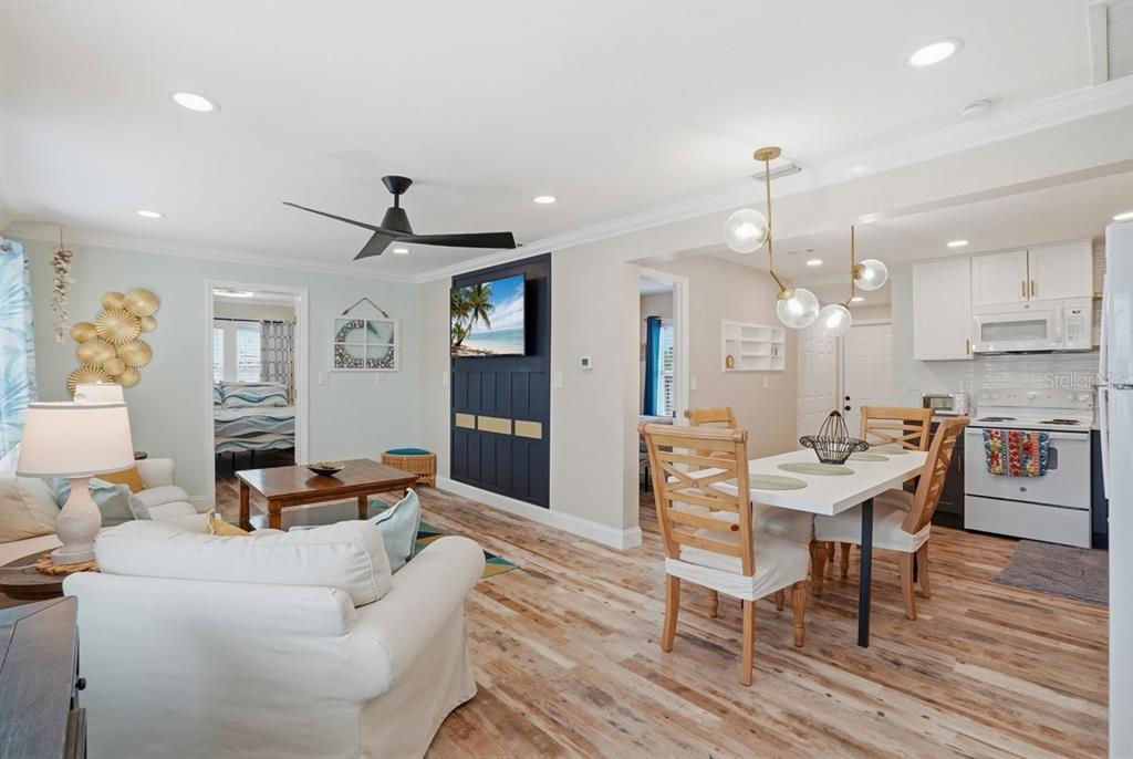An open-concept living and dining area features light wood flooring, white furniture, and a dark accent wall — 118 92ND AVENUE, TREASURE ISLAND, FL