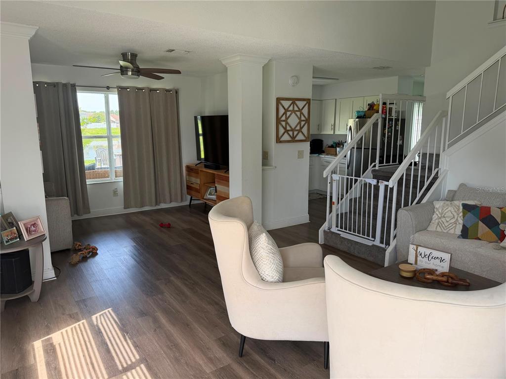 A living room with wood-look flooring, two armchairs, a television, and a staircase with a gate — 9924 SURREY RIDGE ROAD, ORLANDO, FL