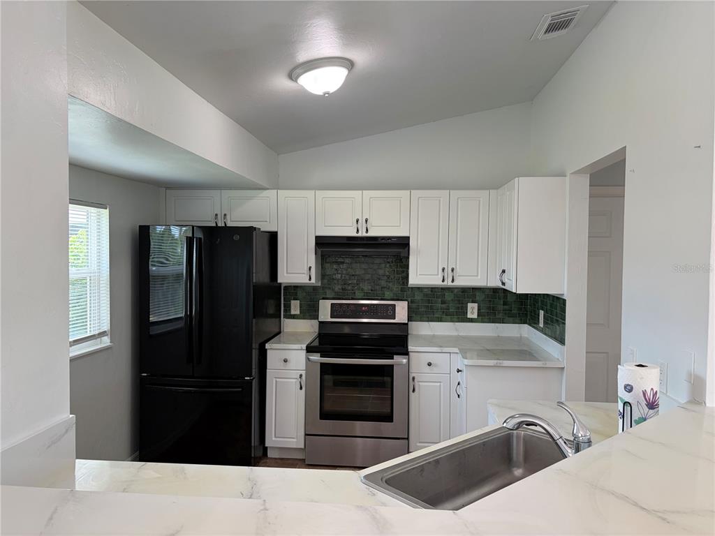 A kitchen features white cabinets, a black refrigerator, a stainless steel stove, and green backsplash — 2723 YACOLT AVENUE, NORTH PORT, FL