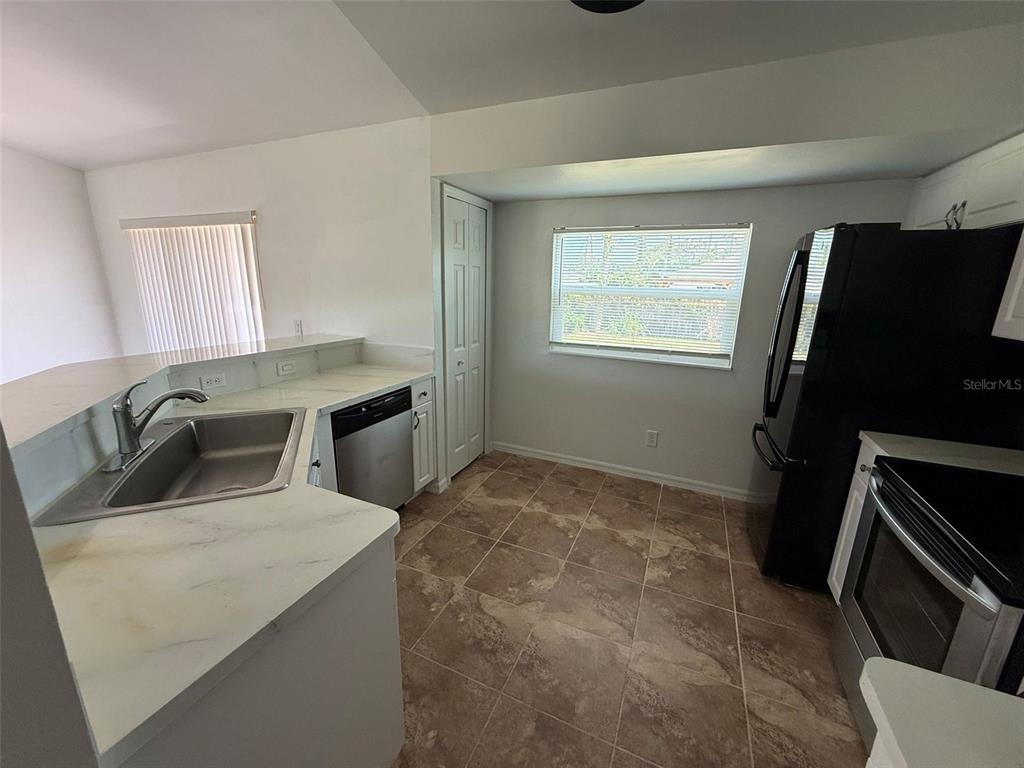 A kitchen features white countertops, stainless steel appliances, tile flooring, and a window with blinds — 2723 YACOLT AVENUE, NORTH PORT, FL