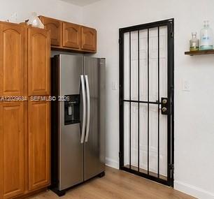 A kitchen features wood cabinets, a stainless steel refrigerator, and a door with security bars — 1020 NW 143rd St, Miami FL 33168, MIAMI, FL