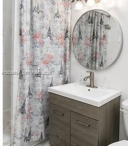 A bathroom features a gray wood vanity, a round mirror, and a Paris-themed shower curtain — 1020 NW 143rd St, Miami FL 33168, MIAMI, FL