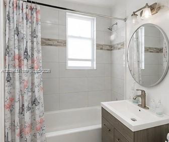 A bathroom with a white tiled tub-shower, a round mirror, and a dark wood vanity — 1020 NW 143rd St, Miami FL 33168, MIAMI, FL
