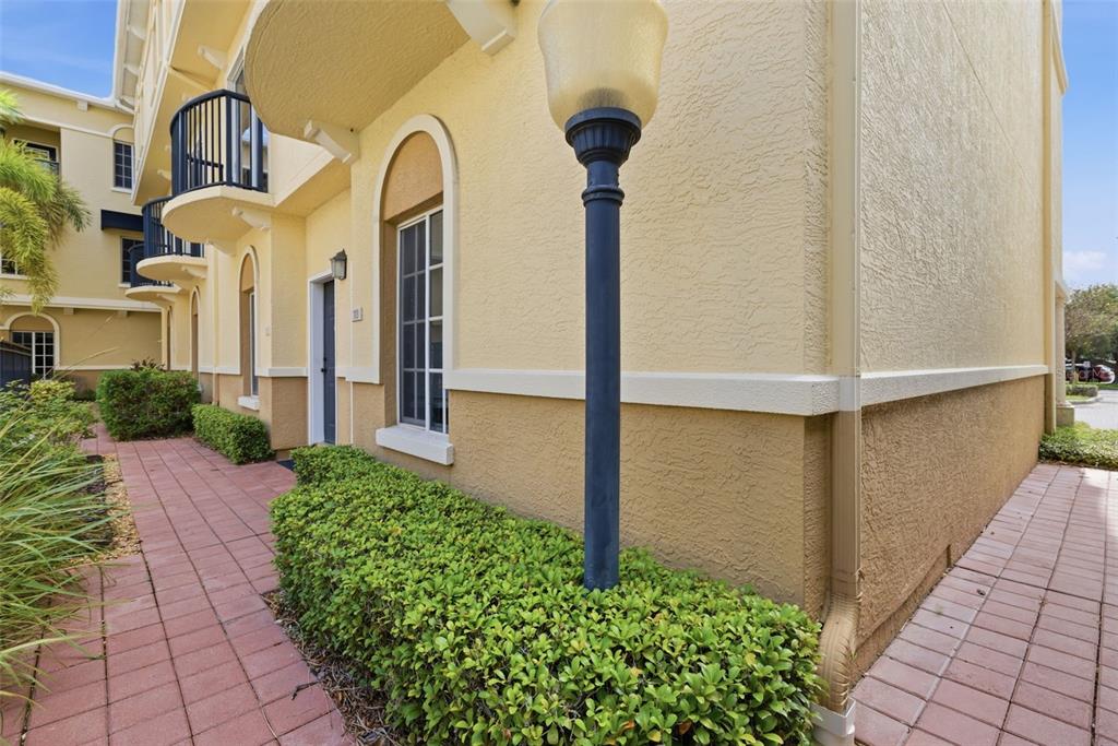 A yellow stucco townhouse exterior features a brick walkway, manicured hedges, and a street lamp — 113 GRAND BEACH PLACE, TAMPA, FL
