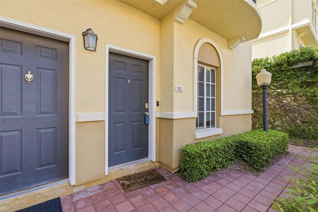 The exterior of a yellow building features two gray doors, a window, and a walkway — 113 GRAND BEACH PLACE, TAMPA, FL