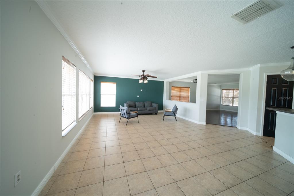 A spacious living room features light tile flooring, a dark accent wall, and large windows — 4621 YELLOW BAY DRIVE, KISSIMMEE, FL