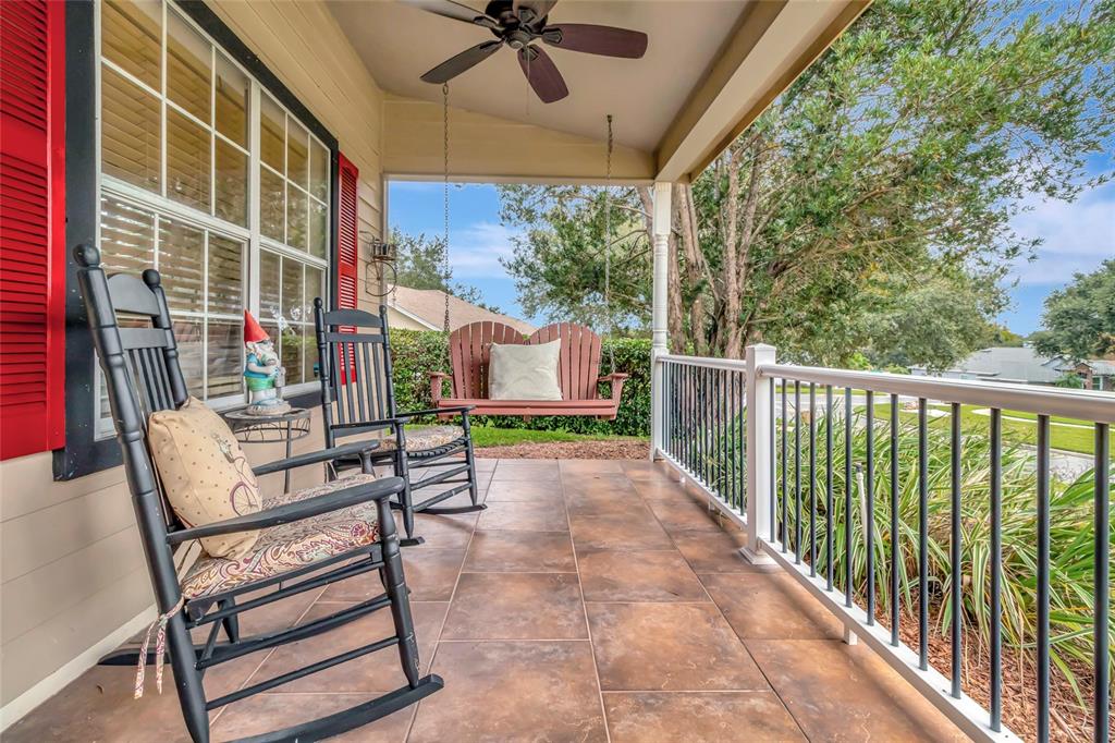A covered porch features tiled flooring, two rocking chairs, and a hanging wooden bench swing — 10414 MESA LANE, CLERMONT, FL