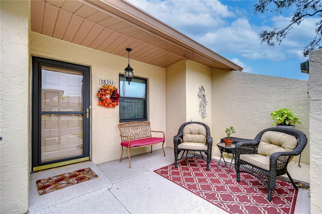 A front porch features a metal bench, a screen door, and a fall-themed wreath — 38351 IRONWOOD PLACE UNIT NA, ZEPHYRHILLS, FL