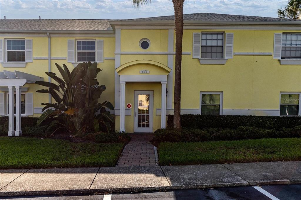 A yellow two-story building features a central entrance with a brick walkway and landscaping — 102 POMPANO DRIVE SE UNIT C, ST PETERSBURG, FL