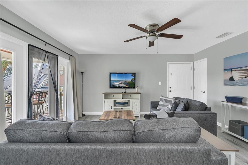 A living room features gray walls, a ceiling fan, a television, and two gray sofas — 102 POMPANO DRIVE SE UNIT C, ST PETERSBURG, FL