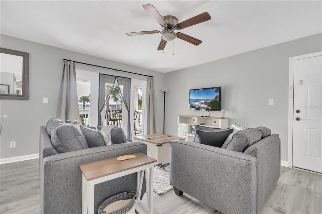 A living room features gray sofas, a ceiling fan, a television, and a balcony door — 102 POMPANO DRIVE SE UNIT C, ST PETERSBURG, FL