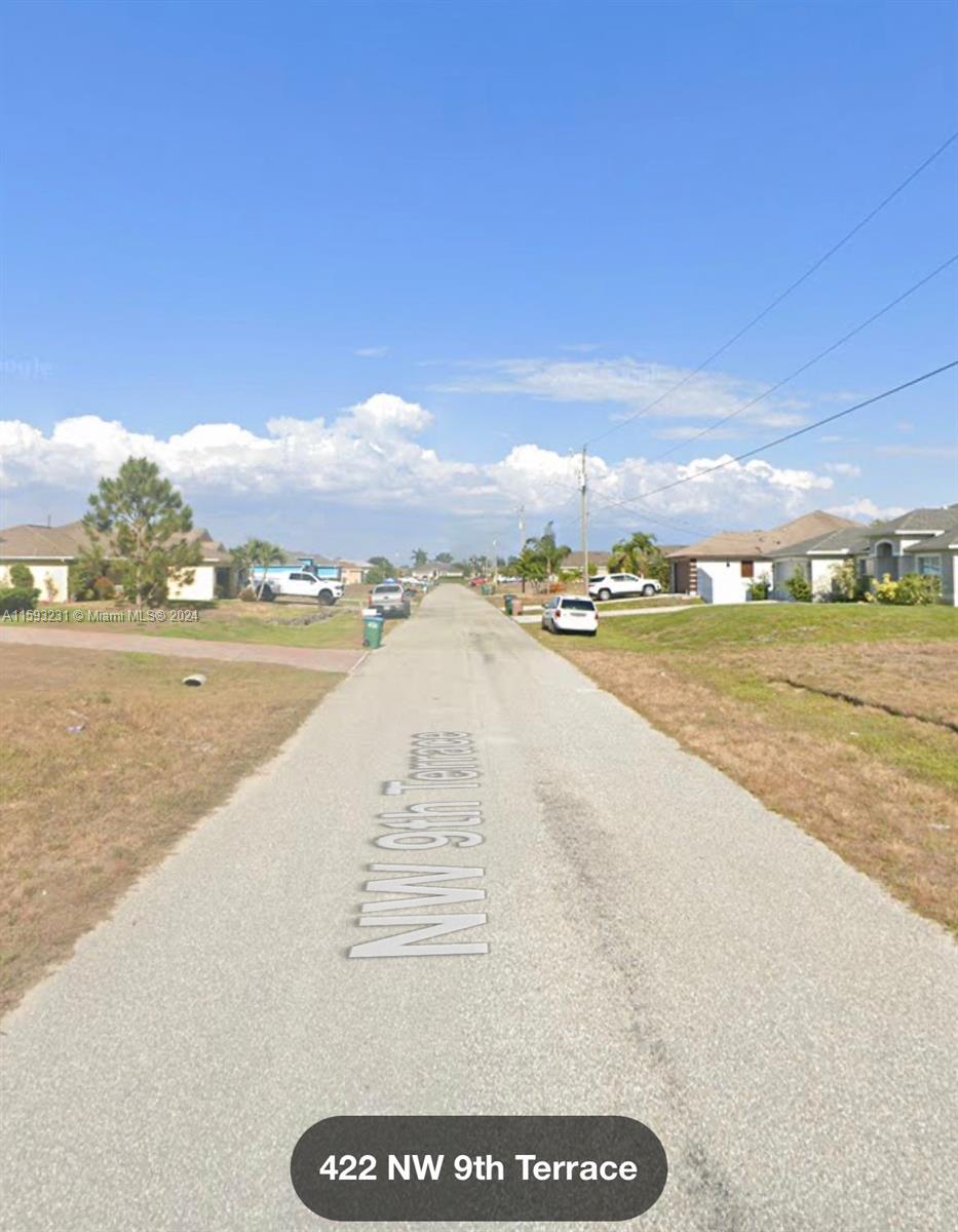 A paved residential street stretches between houses under a clear blue sky — 422 NW 9th Terr, Cape Coral FL 33993, CAPE CORAL, FL