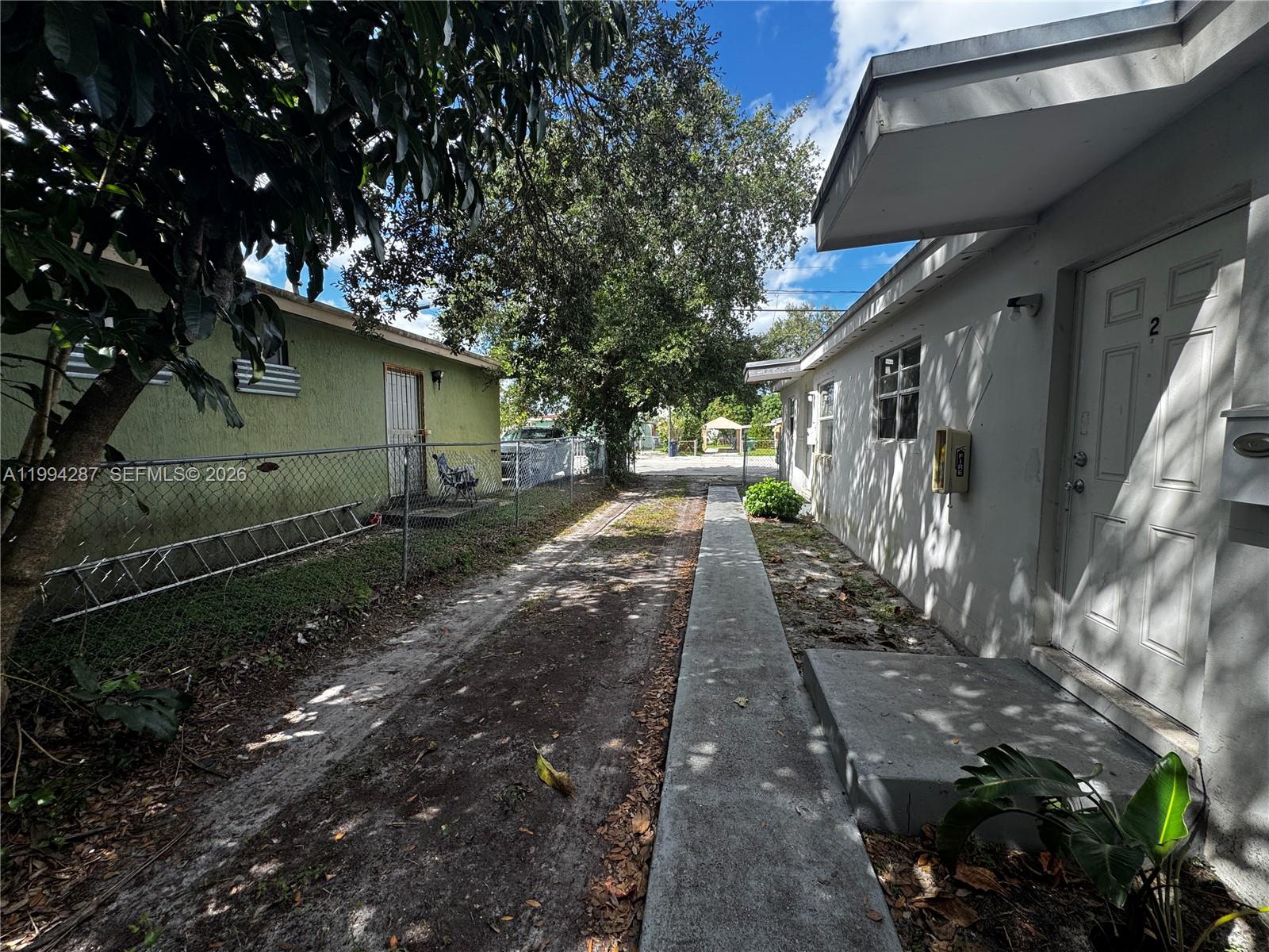 A narrow concrete walkway runs between a white building and a fenced green structure — 1950 Washington Ave # 2, Opa-Locka FL 33054, OPA-LOCKA, FL