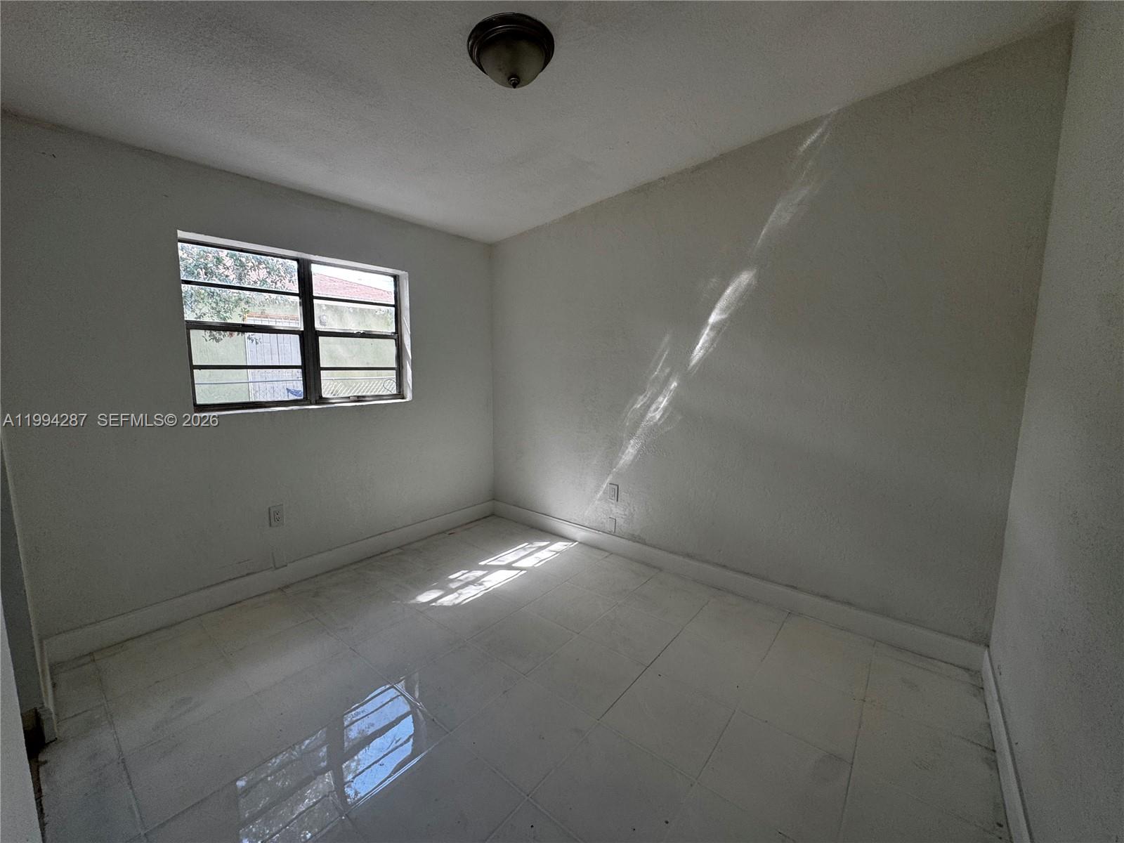 An empty room features white walls, white tile flooring, and a single window — 1950 Washington Ave # 2, Opa-Locka FL 33054, OPA-LOCKA, FL