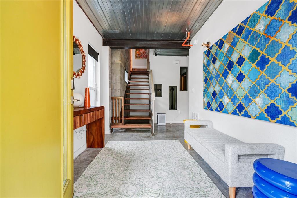 An entryway features a yellow door, a staircase, a large blue wall art, and bench — 1607 WOODWARD STREET UNIT 11, ORLANDO, FL