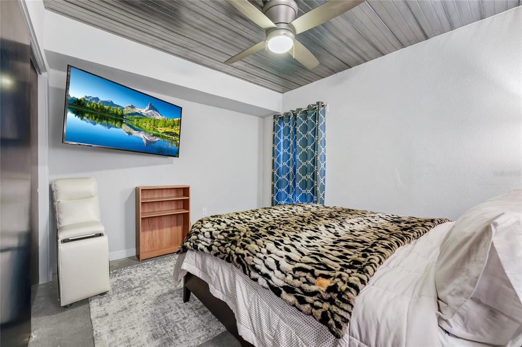 A bedroom features a bed with a leopard print blanket, a wall-mounted television, and ceiling fan — 1607 WOODWARD STREET UNIT 11, ORLANDO, FL