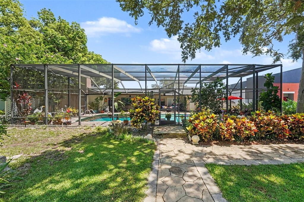 A screened-in swimming pool sits behind a stone walkway and lush landscaping in a backyard — 3061 ALT 19, PALM HARBOR, FL