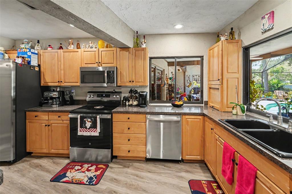 A kitchen with light wood cabinets, stainless steel appliances, and a view of a pool — 3061 ALT 19, PALM HARBOR, FL