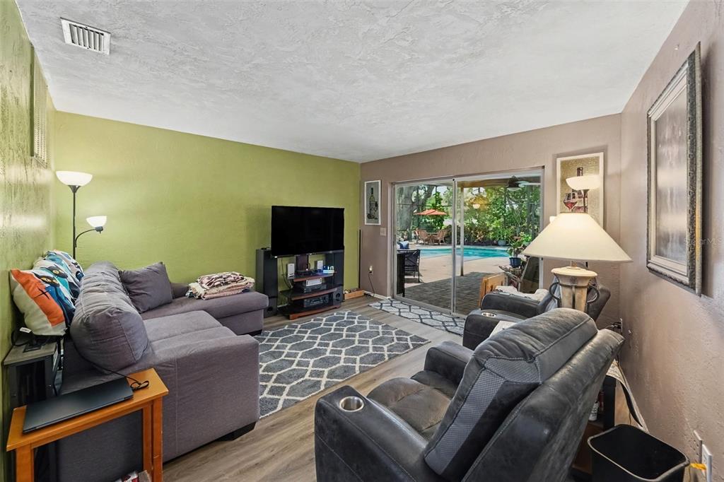 A living room features a grey sectional sofa, a television, and a sliding door to a pool — 3061 ALT 19, PALM HARBOR, FL
