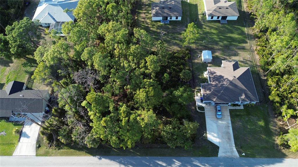 An aerial view shows a wooded lot situated between two residential houses and a street — PETAL ROAD, NORTH PORT, FL