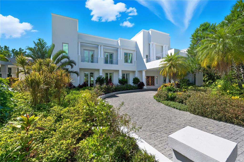 A white two-story modern house features a stone driveway and lush tropical landscaping — 3315 BAY SHORE ROAD, SARASOTA, FL